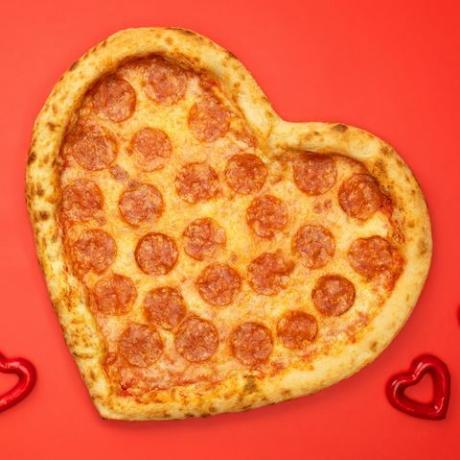 Pizza feferonky ve tvaru srdce na Valentýna na pozadí červeného papíru