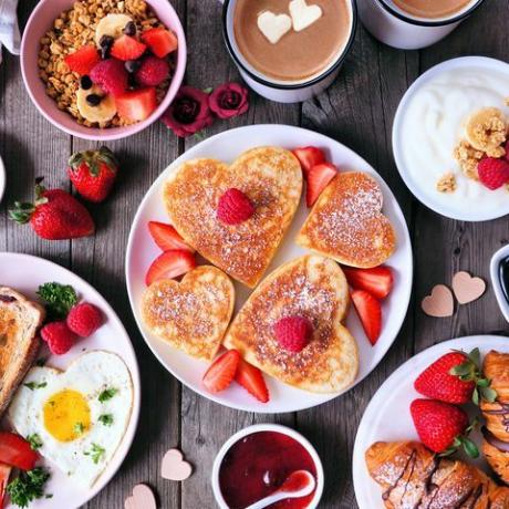 valentýnská scéna se snídaní ke dni matek na tmavém dřevěném pozadí s palačinkami ve tvaru srdce, vejci a jídlem na téma lásky
