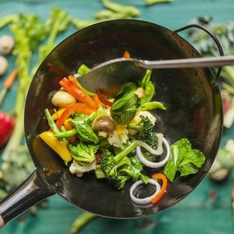 smažení a restování různé čerstvé barevné tržní zeleniny v horkém woku v páře se zeleninou na tyrkysově zbarveném dřevěném pozadí stolu pod wokem